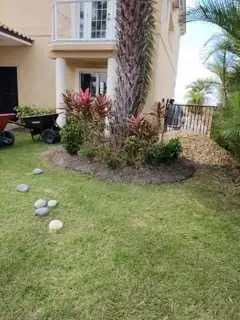 Freshly worked planting bed beside a home with a wheelbarrow on the lawn